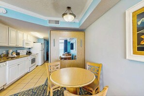 A compact kitchen with white cabinets, a microwave, and a stove. There's a dining area with a round table and chairs. - Paradise Resort 1005 (Myrtle Beach)