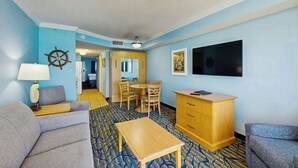 Ett hotellrum med en soffa, ett litet bord, ett träskåp, en tv och en skeppsratt som dekoration på väggen.