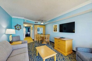 A hotel room with a sofa, a small table, a wooden cabinet, a television, and a ship's wheel decoration on the wall. - Paradise Resort 1005 (Myrtle Beach)