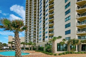 A high-rise hotel with multiple balconies, a swimming pool, and palm trees. - Palace Resort Unit 710 (Myrtle Beach)