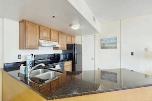 A kitchen with wooden cabinets, a stainless steel sink, a black refrigerator, and a microwave. - Palace Resort Unit 710 (Myrtle Beach)