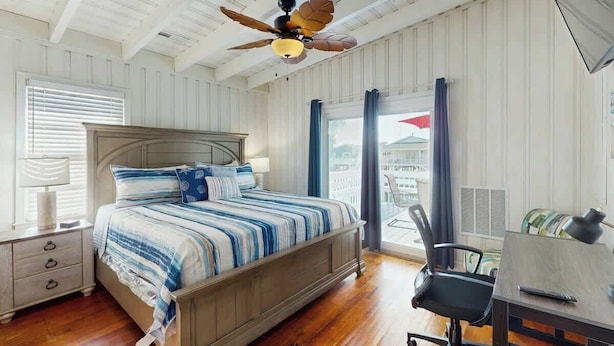 A bedroom with a bed, a desk, a chair, a ceiling fan, and a window with curtains. - Casa del Mare Beach House (North Myrtle Beach)