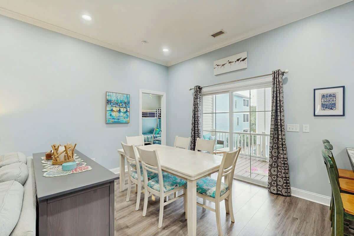 A dining area with a table and chairs, a small kitchen area, and a view through a glass door.