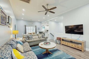 Ein modernes Wohnzimmer mit Sofa, Couchtisch, Fernseher und Deckenventilator.