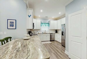 A kitchen with white cabinets, a marble island, and a stainless steel refrigerator. - Hello Sunshine Beach House (North Myrtle Beach)