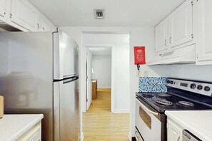 Una cocina con armarios blancos, un refrigerador de acero inoxidable, una estufa negra y un salpicadero de azulejos.
