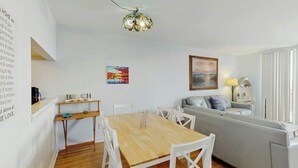 Ein modernes Wohnzimmer mit einem Holzes Esstisch, weißen Stühlen, einem grauen Sofa und einer Deckenleuchte.