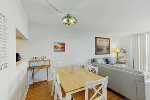 Ein modernes Wohnzimmer mit einem Holzes Esstisch, weißen Stühlen, einem grauen Sofa und einer Deckenleuchte.