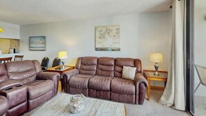 A hotel room with a leather sofa, a coffee table, a lamp, and a painting on the wall. - Holiday Towers Unit 501 (Myrtle Beach)