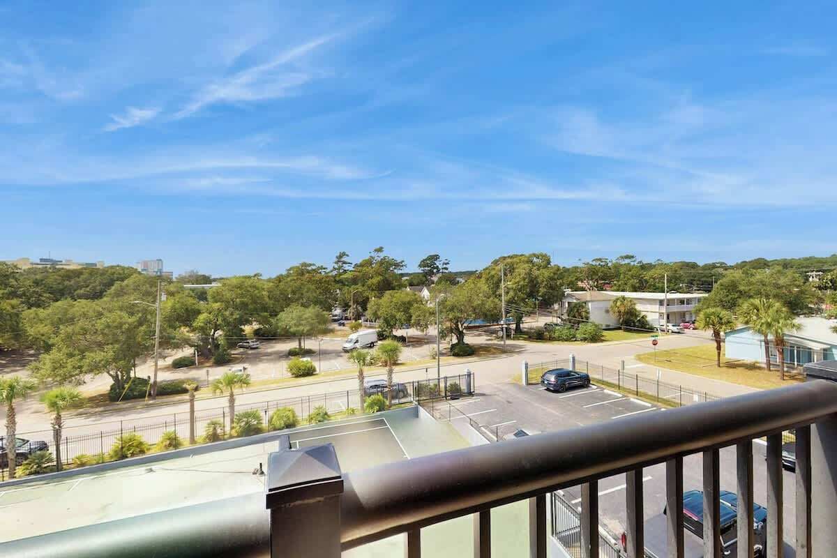 Blick vom Balkon auf einen Parkplatz mit Bäumen und Gebäuden im Hintergrund.