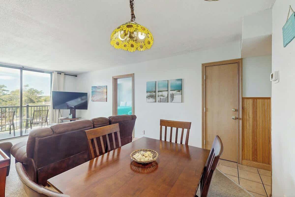 A dining area with a wooden table, chairs, a television, and a large window.