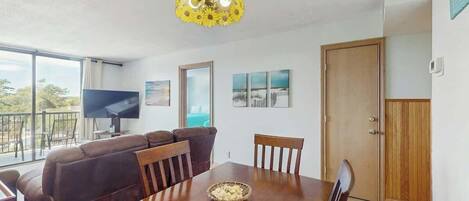 A dining area with a wooden table, chairs, a television, and a large window.