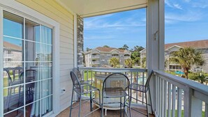 A balcony with a table and chairs, overlooking a pool and other buildings. - Wild Iris Unit 202 Condo (Myrtle Beach)
