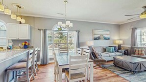 A spacious living area with a dining table, sofas, and a kitchen area with cabinets and a window. - Wild Iris Unit 202 Condo (Myrtle Beach)