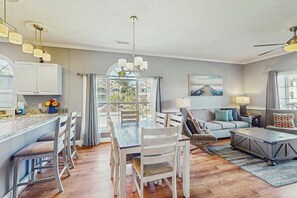 A spacious living area with a dining table, sofas, and a kitchen area with cabinets and a window. - Wild Iris Unit 202 Condo (Myrtle Beach)