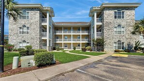 A multi-story building with a central courtyard, balconies, and a parking lot. - Wild Iris Unit 202 Condo (Myrtle Beach)
