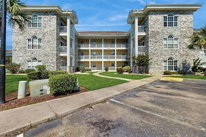 A multi-story building with a central courtyard, balconies, and a parking lot. - Wild Iris Unit 202 Condo (Myrtle Beach)