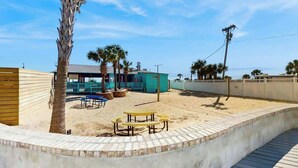 A beachside property with a fenced patio area, outdoor seating, and a building with a green roof. - Beyond the Blue Retreat (Myrtle Beach)