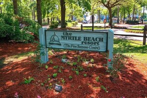 A sign for the Myrtle Beach Resort with a bell graphic, surrounded by mulch and small plants. - Beyond the Blue Retreat (Myrtle Beach)