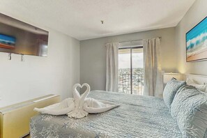 Quarto de hotel com uma cama, janela com cortinas, televisão de tela plana na parede e um quadro na parede.