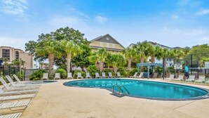 A swimming pool with lounge chairs, palm trees, and a building in the background. - Holiday Towers Unit 1108 (Myrtle Beach)