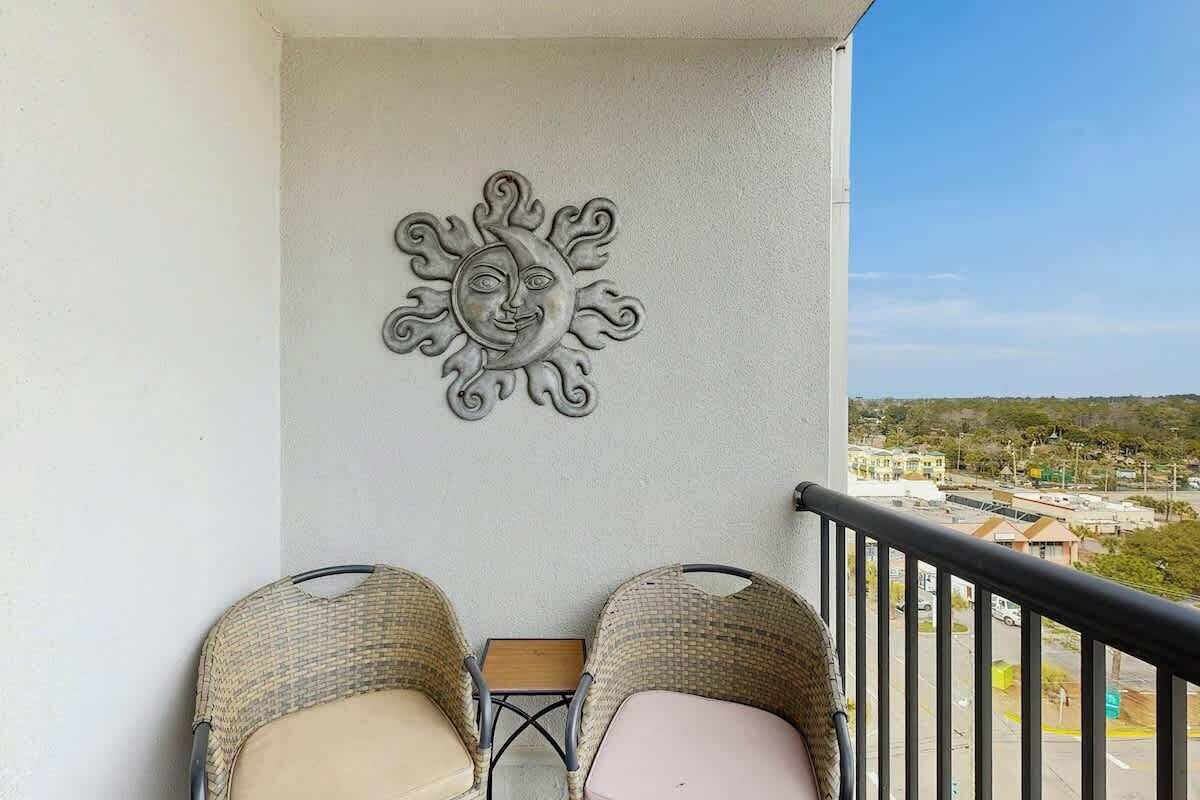 A balcony with wicker chairs, a small table, and a decorative sun wall.