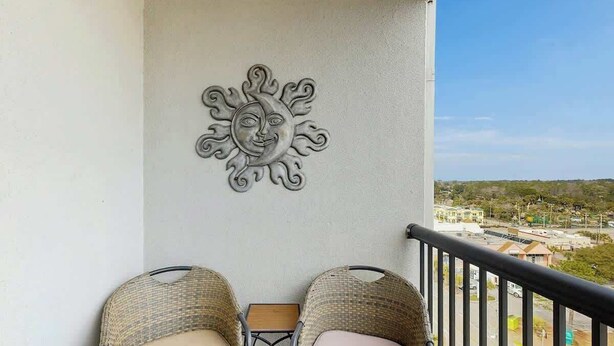A balcony with wicker chairs, a small table, and a decorative sun wall. - Holiday Towers Unit 1108 (Myrtle Beach)