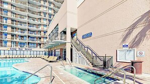A hotel pool area with multiple swimming pools, a staircase leading to a balcony, and a sign indicating a no-smoking policy. - Grande Cayman Unit 413 (Myrtle Beach)
