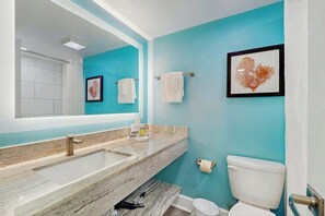 Ein Badezimmer mit großem Spiegel, Waschbecken, Toilette und einem gerahmten Kunstwerk an der Wand.