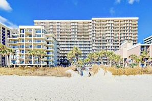Ein Hotel direkt am Strand mit mehreren Etagen, Balkonen und Palmen.