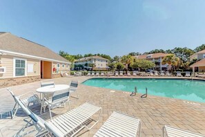 Ein Poolbereich mit Liegestühlen und einem Tisch, umgeben von Gebäuden mit Balkonen.