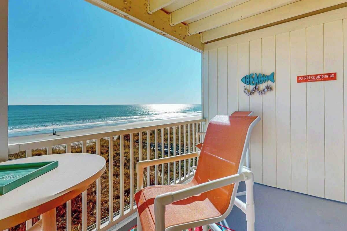 Ein Balkon mit Blick auf den Strand, ein Stuhl und ein Tisch.