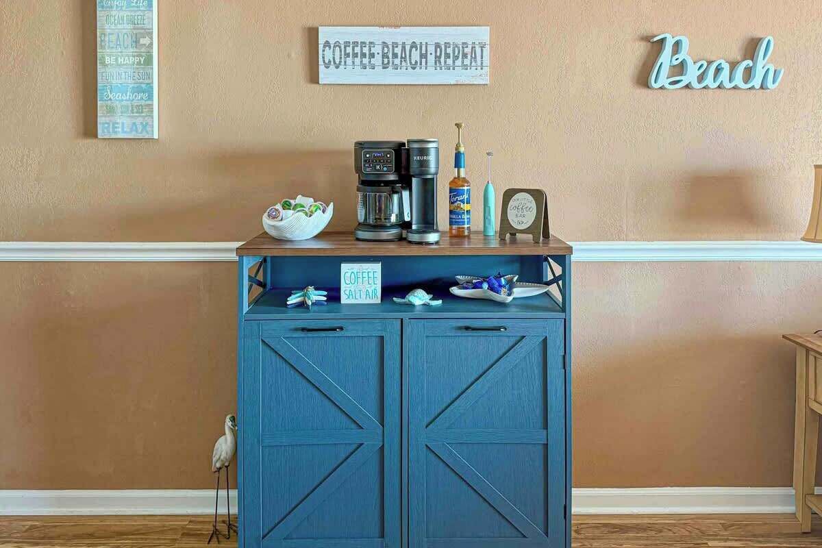 A coffee station with a coffee maker, a salt shaker, and a coffee mug on a blue cabinet against a beige wall.
