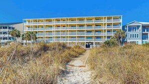 A multi-story hotel with a central entrance, surrounded by beach vegetation. - Windy Shores II - 305 (North Myrtle Beach)