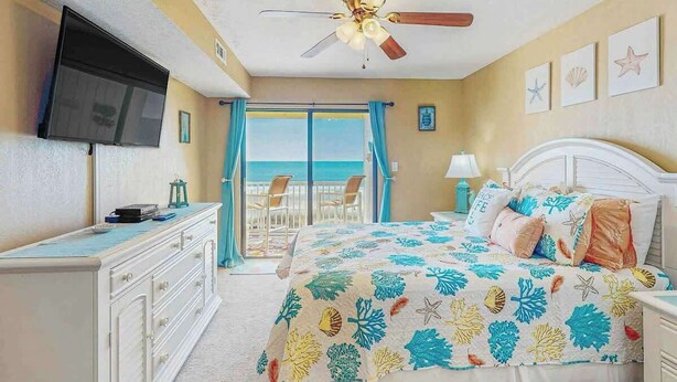 A bedroom with a bed, a TV, a ceiling fan, and a view of the ocean. - Windy Shores II - 305 (North Myrtle Beach)