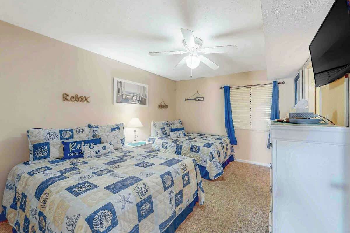Un dormitorio con dos camas, ventilador de techo, televisor y refrigerador.
