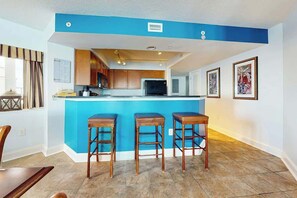 A compact kitchen with a central island, wooden stools, and a blue accent wall. - Bahama Sands Unit PH09 (North Myrtle Beach)