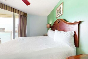 A hotel room with a large bed, a nightstand, a lamp, and a view of the outside. - Bahama Sands Unit PH09 (North Myrtle Beach)