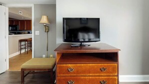 Uma televisão sobre um suporte de madeira em um quarto com um banco e um abajur.