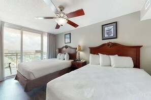 A hotel room with two beds, a ceiling fan, a window with a view, and a framed picture on the wall. - Bahama Sands Unit 1210 (North Myrtle Beach)