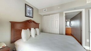Quarto com cama grande, cabeceira de madeira, mesa de cabeceira e um quadro na parede.