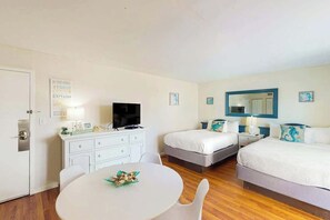 Ein Hotelzimmer mit zwei Betten, einem Fernseher, einem Schreibtisch mit Stuhl und einem runden Tisch.
