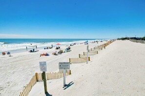Ein Sandstrand mit einer Holzzaun und Schildern, im Hintergrund das Meer.