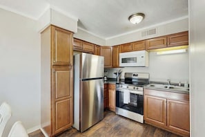 Eine Küche mit Holzausstattung, einem Edelstahlkühlschrank, einer Mikrowelle, einem Backofen und einem Spülbecken.