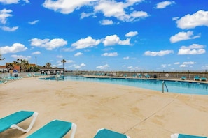 Ein Swimmingpool mit Liegestühlen, einem klaren Himmel und weiter Blick auf einen Strand.