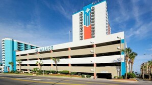 Un parking à étages, avec une grande enseigne « PALACE » bien visible, situé à côté d’un immeuble de grande hauteur aux couleurs bleue et blanche.