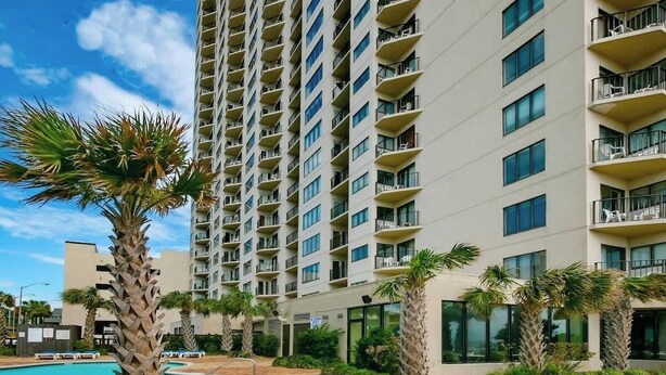 Un hôtel de grande hauteur doté de nombreux balcons, d’une piscine et de palmiers.