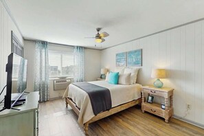 Ein Schlafzimmer mit Bett, Nachttischen, Deckenventilator und einem fensterbepflanzten Fenster.