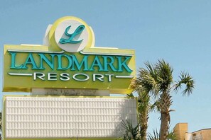 A LANDMARK RESORT sign with a prominent 'L' logo, a clear sky, and palm trees in the background. - Landmark Resort Unit 920 (Myrtle Beach)