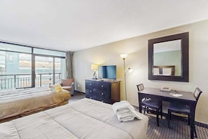 A hotel room with a bed, a desk, a chair, a TV, and a large window. - Landmark Resort Unit 920 (Myrtle Beach)